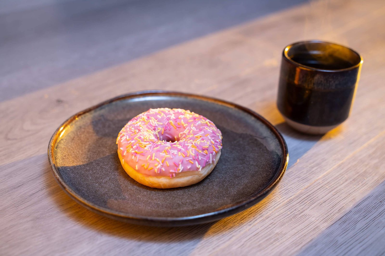 Studio photo of a pink-iced donut on a plate next to a cup